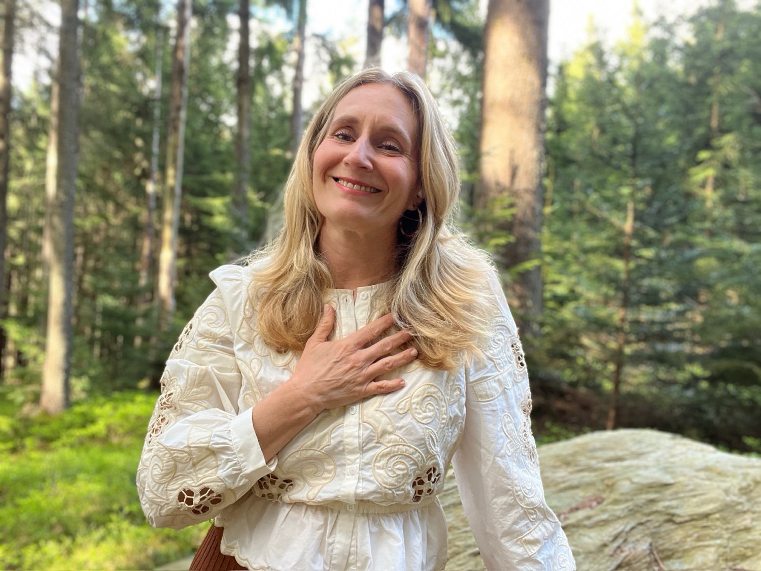 Michaela Christine Wolf, founder of The Here & Now, in a forest with her hand on her heart